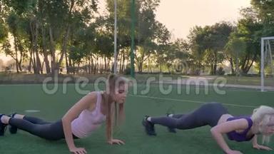 两名年轻女子在公园的足球场上伸展身体，减肥，健身模特运动